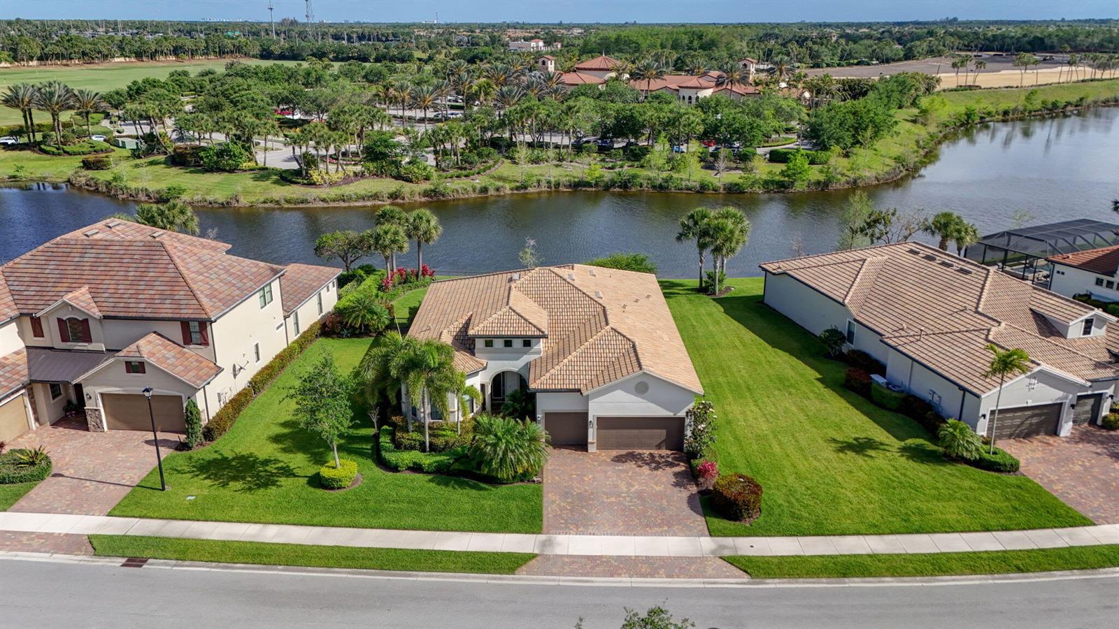 An aerial view shows three suburban houses with tile roofs situated along a lake — 532 Sonoma Isles Circle, Jupiter FL 33478, JUPITER, FL