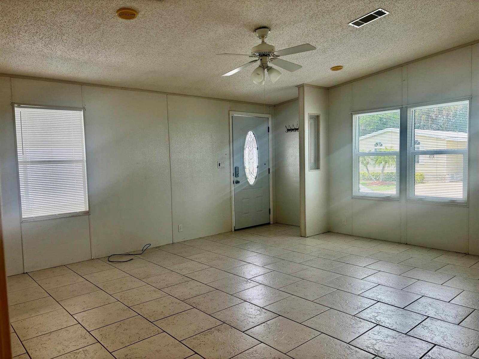 An empty living room features white paneled walls, light-colored tile flooring, and a ceiling fan — 1586 SW 35th Circle, Okeechobee FL 34974, OKEECHOBEE, FL