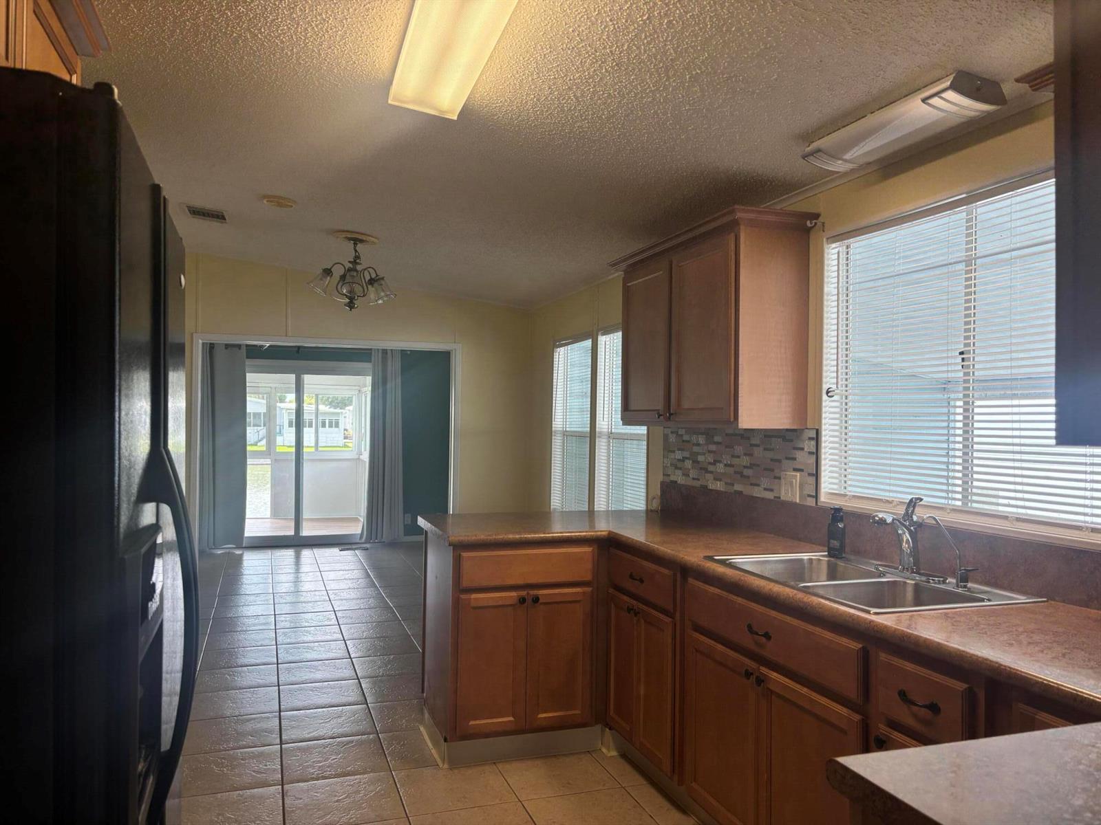 A kitchen with wood cabinets, laminate countertops, and tile flooring overlooks a sunroom — 1586 SW 35th Circle, Okeechobee FL 34974, OKEECHOBEE, FL