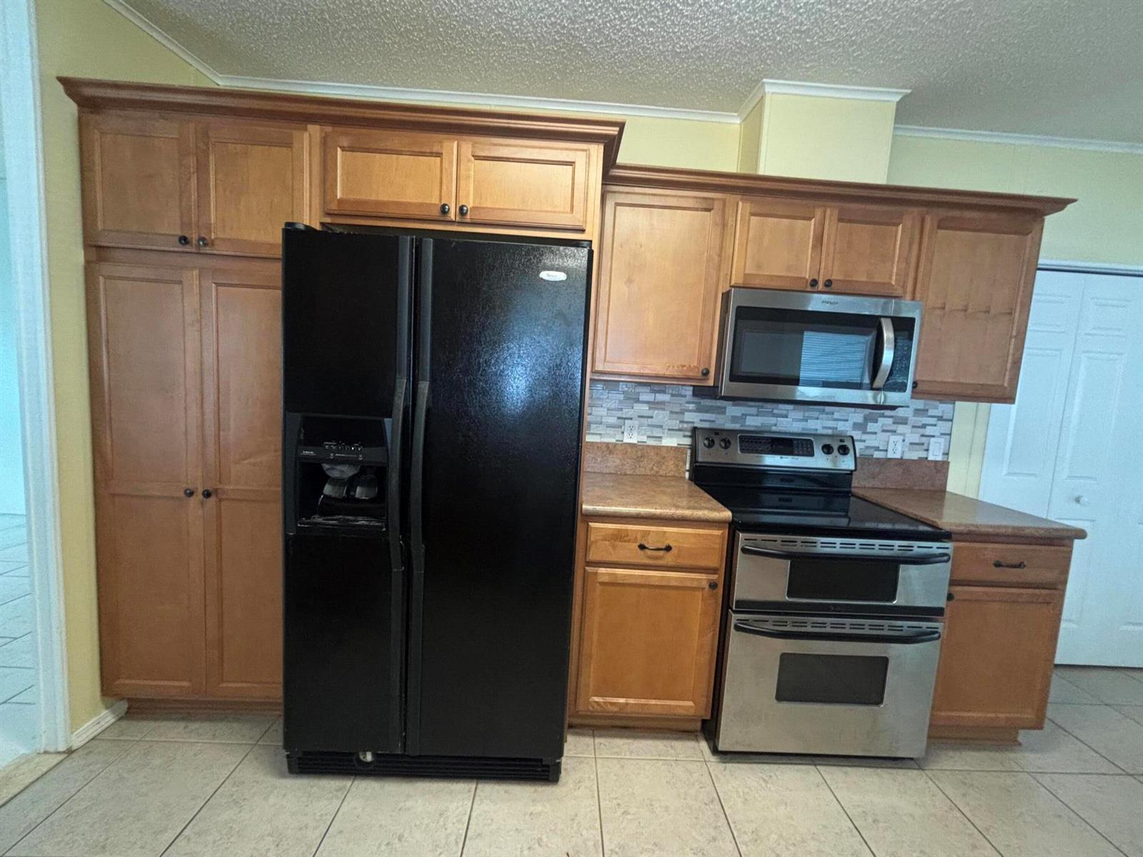 A kitchen features wooden cabinets, a black refrigerator, and stainless steel appliances — 1586 SW 35th Circle, Okeechobee FL 34974, OKEECHOBEE, FL