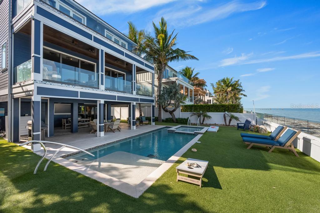 An aerial view shows a multi-story blue house with a pool along a sandy beach — 915 N SHORE DRIVE, ANNA MARIA, FL