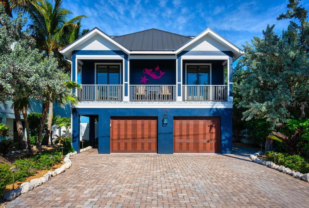 An aerial view shows a blue multi-story house with a metal roof facing the ocean — 915 N SHORE DRIVE, ANNA MARIA, FL