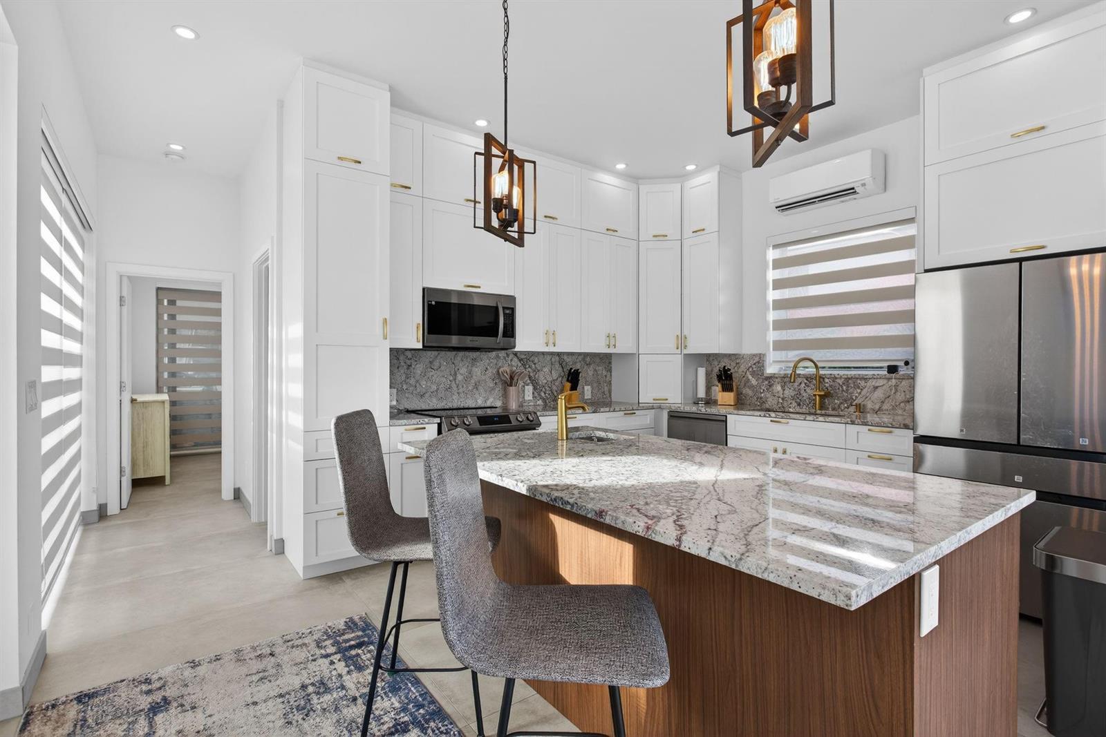 A modern kitchen features white cabinetry, a granite-topped island, and two gray bar stools — 633 N Cortez Drive # 633, Margate FL 33068, MARGATE, FL
