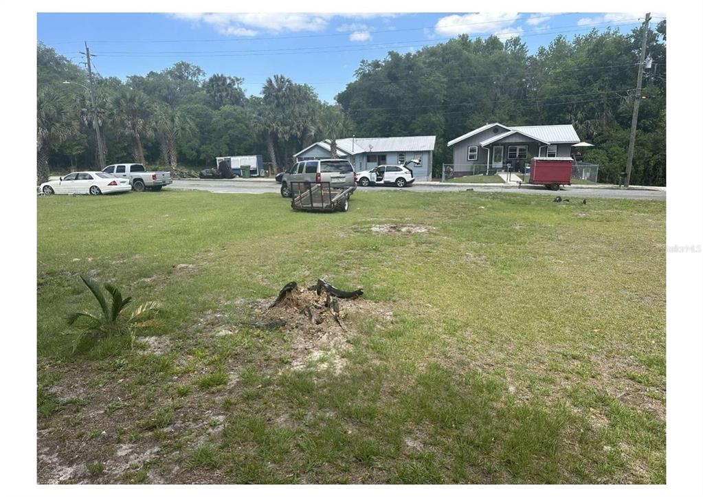 A grassy vacant lot with a tree stump in the foreground and houses across the street — 1206 S 12TH STREET, PALATKA, FL