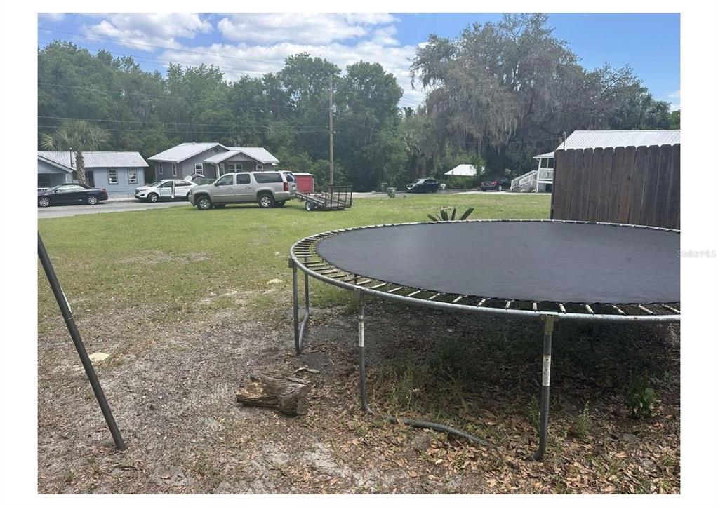 A backyard features a large trampoline on a grassy lot with nearby houses and vehicles — 1206 S 12TH STREET, PALATKA, FL