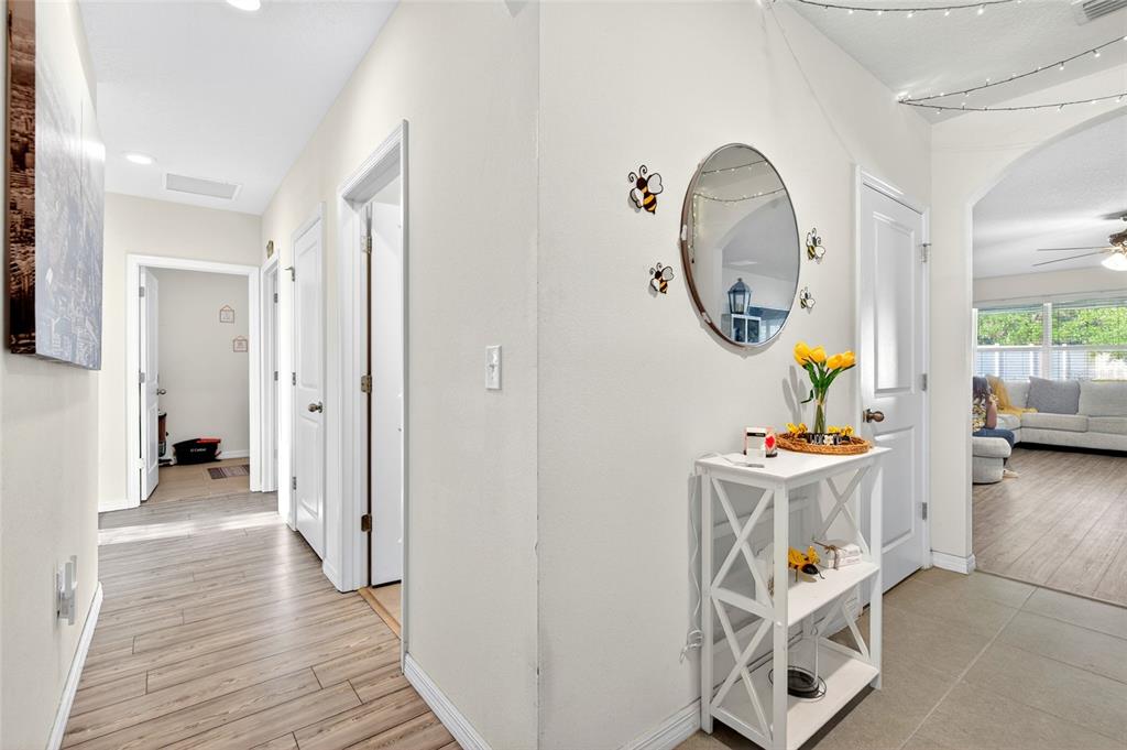 A hallway with wood-look flooring leads to a white console table with a round mirror — 2579 NE 46TH AVENUE, OCALA, FL