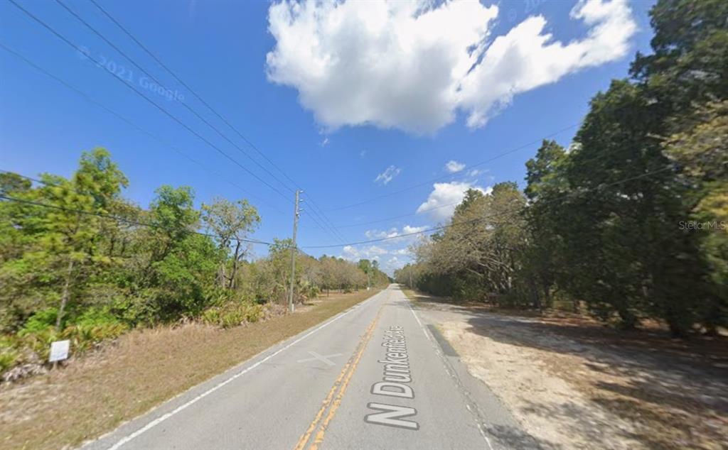 A paved road stretches through a wooded area under a blue sky with clouds — 632 N DUNKENFIELD AVENUE, CRYSTAL RIVER, FL