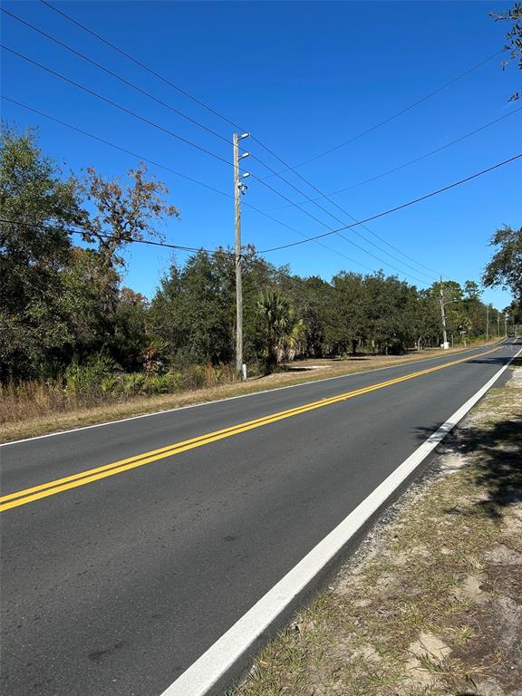 A paved two-lane road stretches past a utility pole and a wooded area under blue skies — 632 N DUNKENFIELD AVENUE, CRYSTAL RIVER, FL