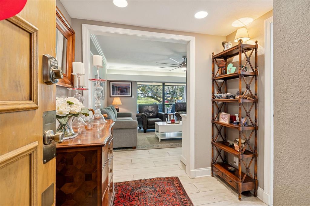 An entryway with a wooden dresser and tall shelving leads into a living room area — 36750 US HIGHWAY 19 N UNIT 16210, PALM HARBOR, FL