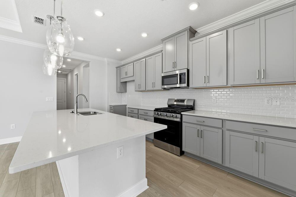 A modern kitchen features gray cabinets, white countertops, a central island, and stainless steel appliances — 7731 CASPIAN STREET, PALMETTO, FL