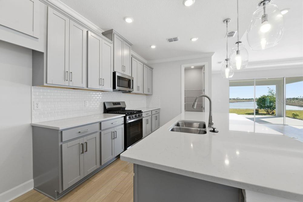 A modern kitchen features gray cabinets, white quartz countertops, a large island, and stainless appliances — 7731 CASPIAN STREET, PALMETTO, FL