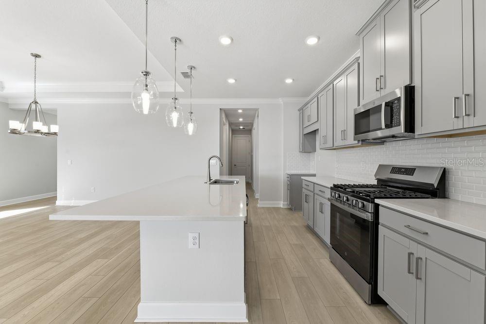 A modern kitchen features gray cabinets, a white quartz island, and light wood-look flooring — 7731 CASPIAN STREET, PALMETTO, FL