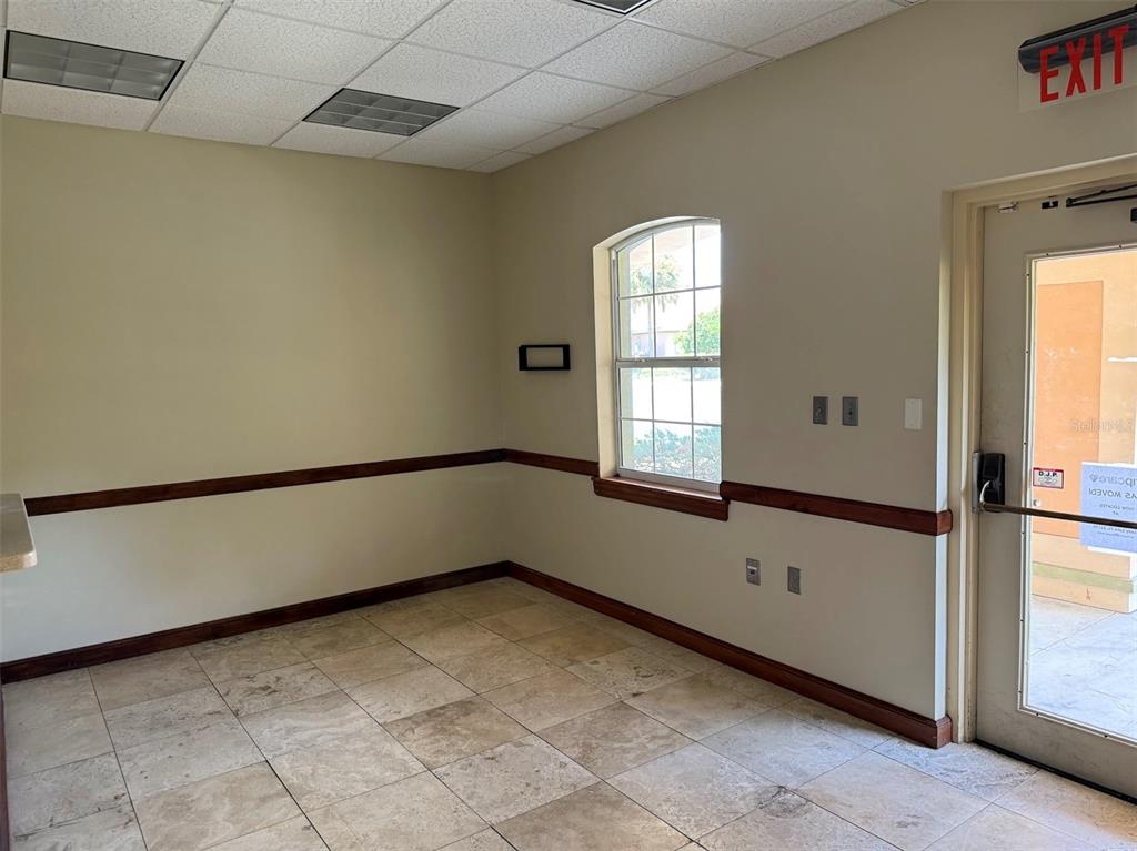 An empty office room features beige walls, a tiled floor, a window, and an exit door — 1400 S US HWY 441, BUILDING 910 UNIT 912, LADY LAKE, FL
