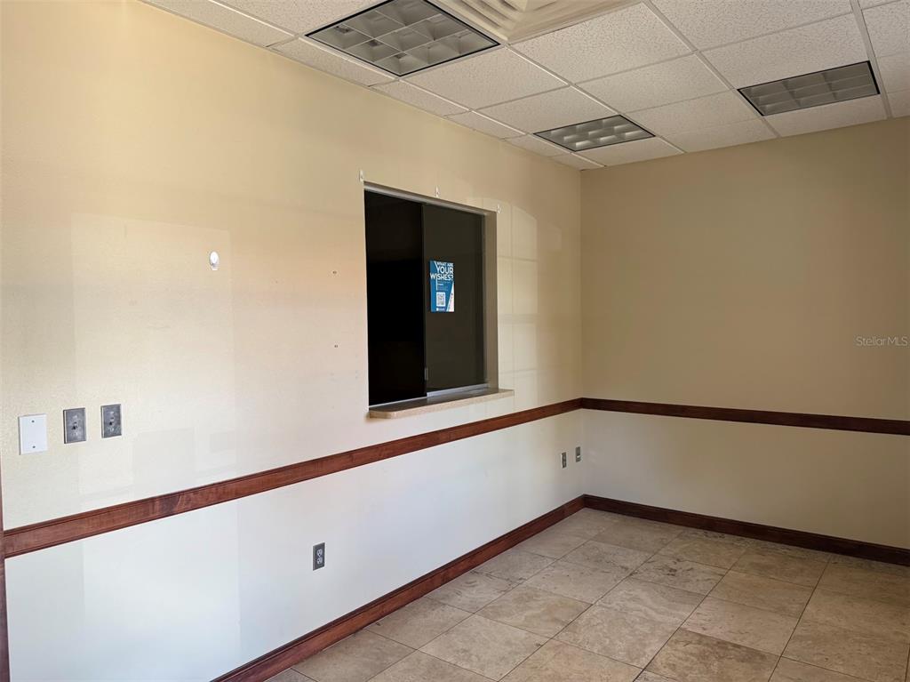 An empty office room features beige walls, a service window, chair rail molding, and tile flooring — 1400 S US HWY 441, BUILDING 910 UNIT 912, LADY LAKE, FL