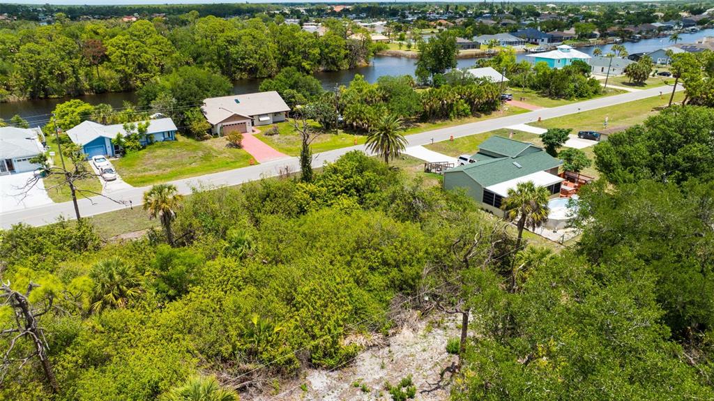 An aerial view shows a vacant, wooded lot situated between several residential houses and canals — 12047 CHANCELLOR BOULEVARD, PORT CHARLOTTE, FL