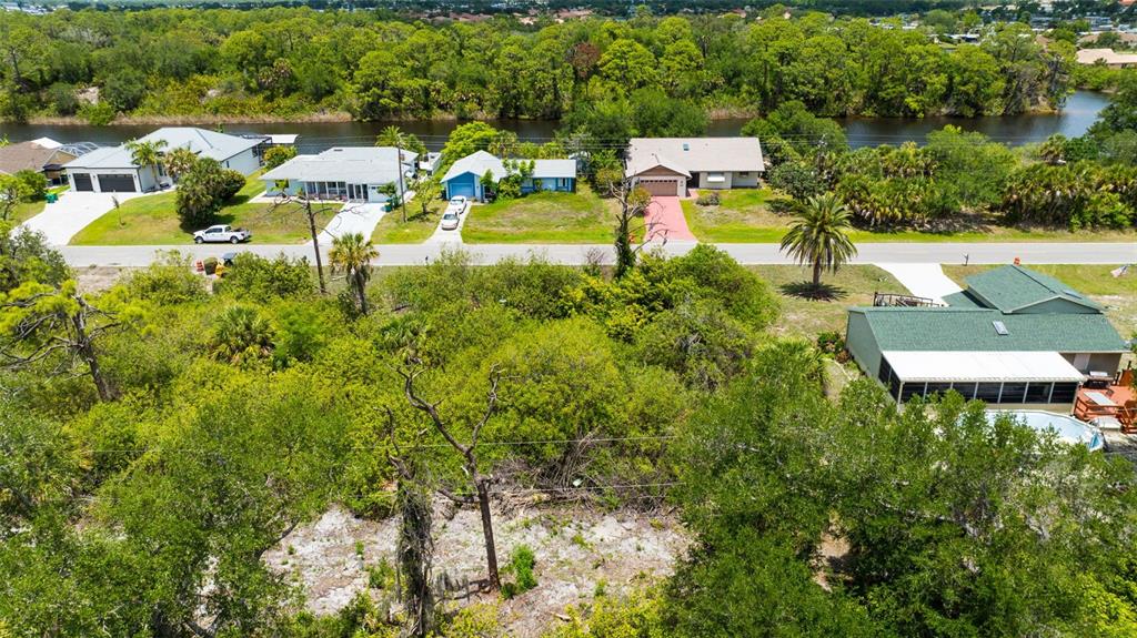 An aerial view shows a vacant, tree-covered lot situated across the street from waterfront homes — 12047 CHANCELLOR BOULEVARD, PORT CHARLOTTE, FL