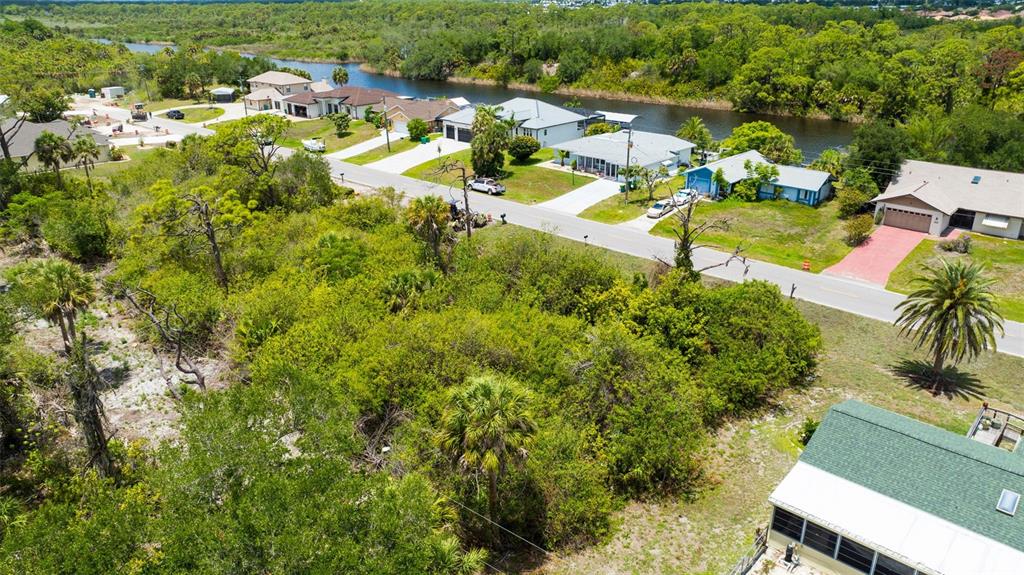 An aerial view shows a vacant, wooded lot situated between residential homes and a canal — 12047 CHANCELLOR BOULEVARD, PORT CHARLOTTE, FL