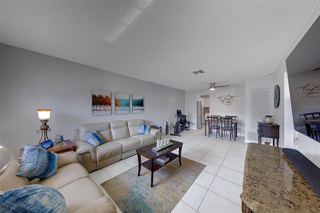 A living room with light-colored tile floors, a beige sofa, and a dining area — 9906 LILY STREET N, PINELLAS PARK, FL