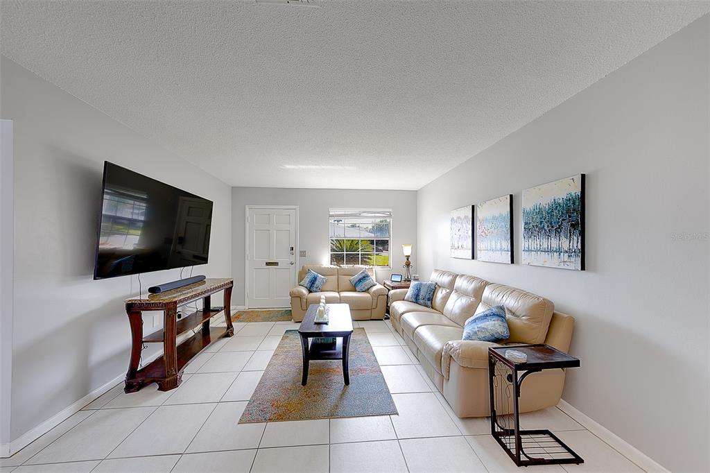A living room features light tile floors, a large television, and beige leather seating — 9906 LILY STREET N, PINELLAS PARK, FL