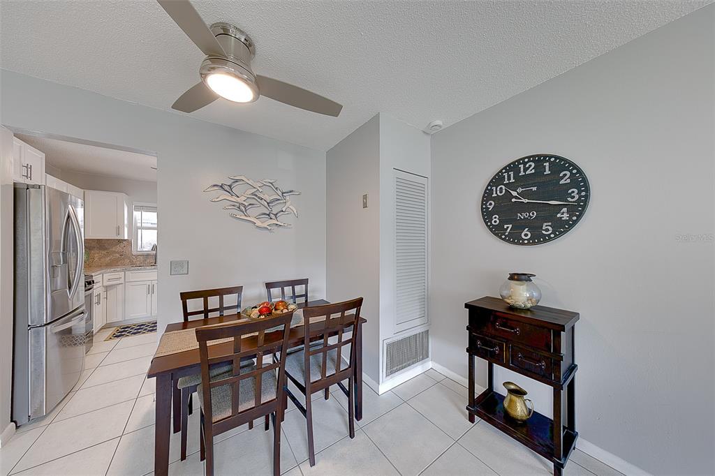 A dining area features a wooden table, four chairs, a console table, and a wall clock — 9906 LILY STREET N, PINELLAS PARK, FL