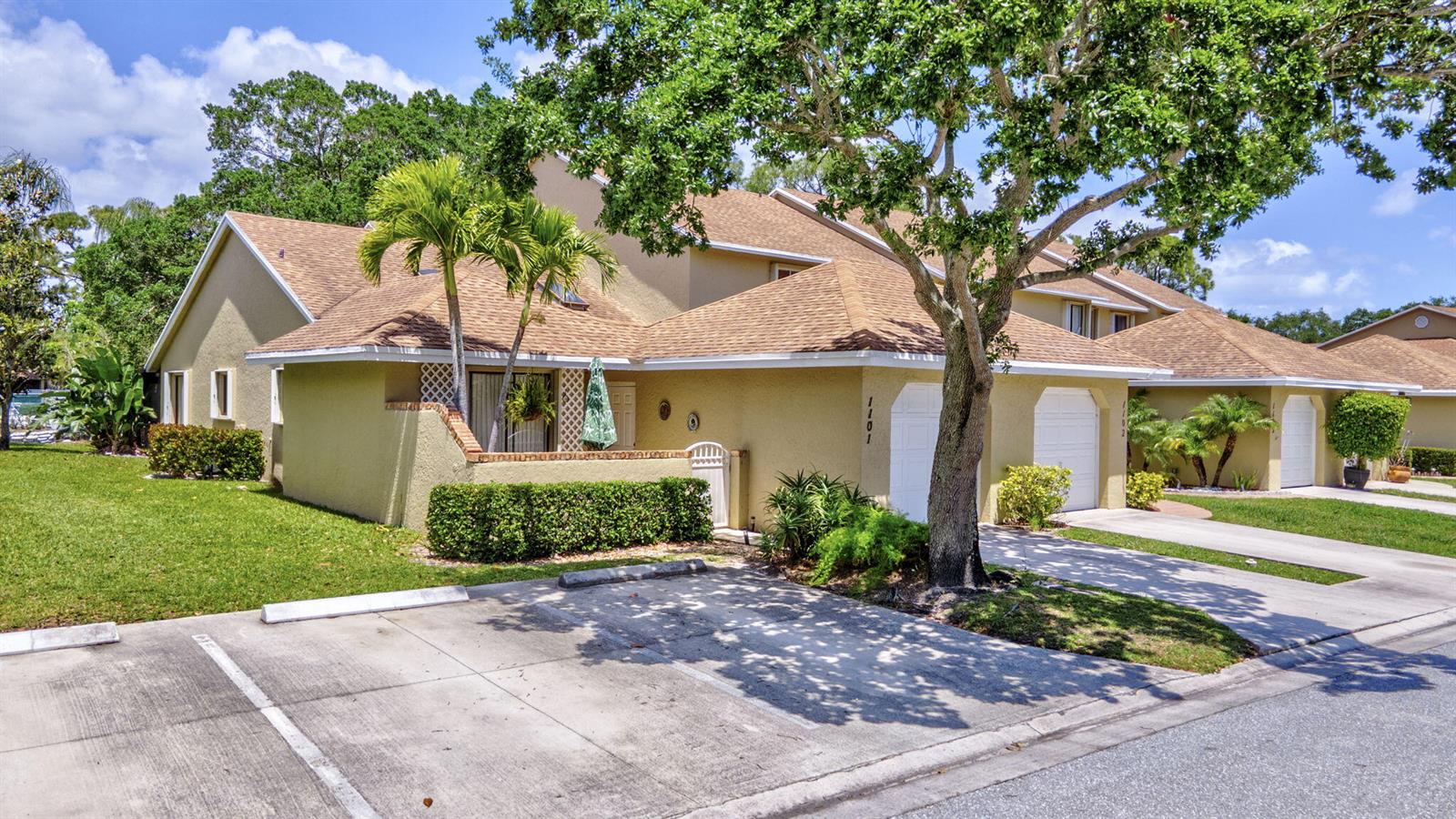 A tan townhouse with a brown shingled roof, a garage, and a small front patio — 1101 Maplewood Drive, FL 33415, FL