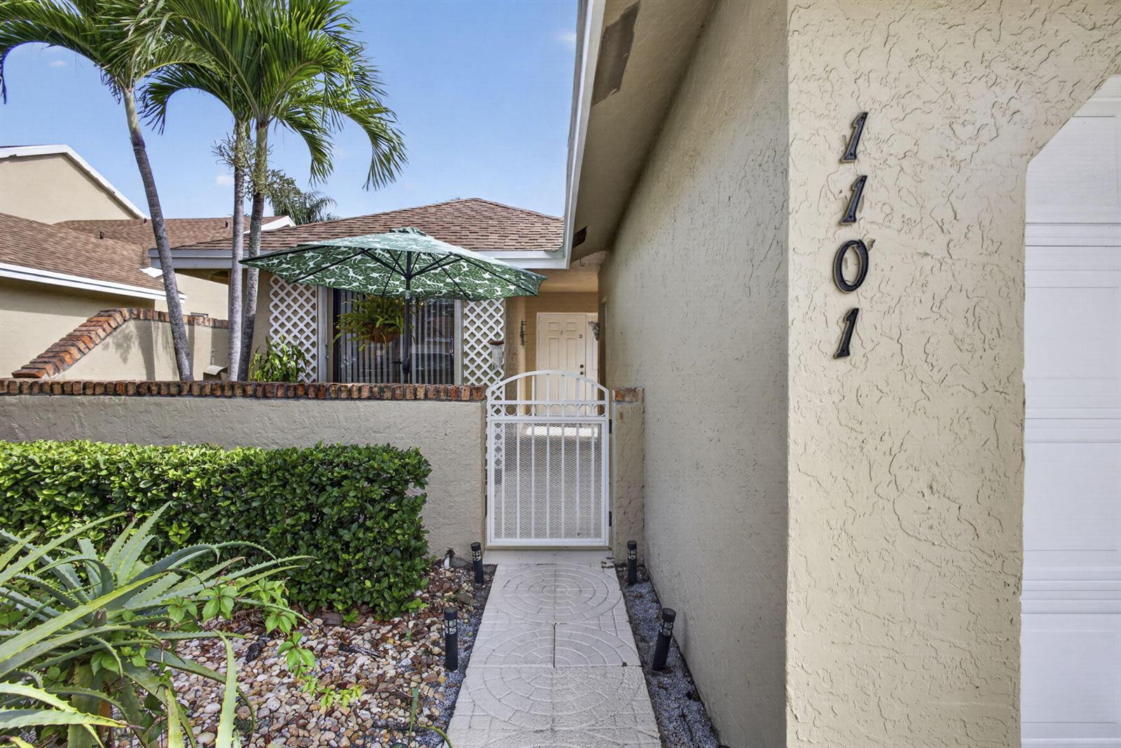 A white gate leads to a front entrance with a stone walkway and house numbers — 1101 Maplewood Drive, FL 33415, FL