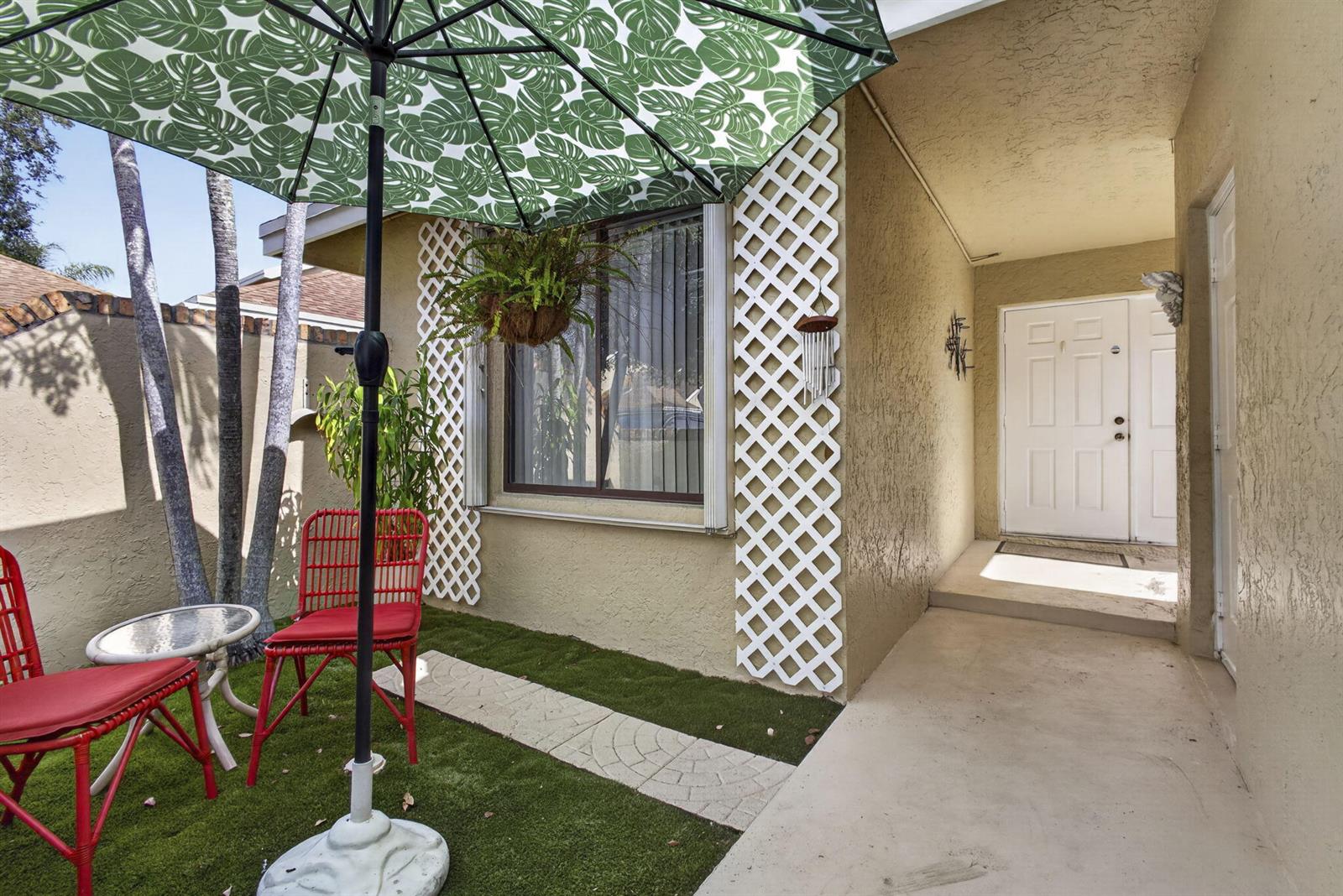 A patio area features artificial turf, red chairs, a small table, and a green umbrella — 1101 Maplewood Drive, FL 33415, FL