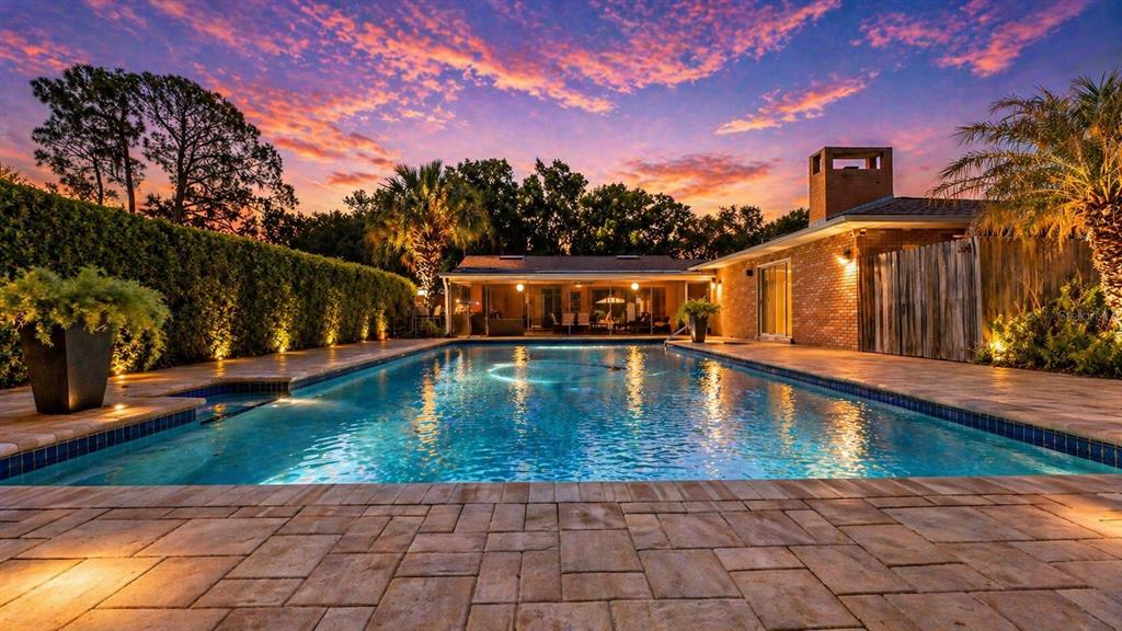 A swimming pool sits in front of a brick house at sunset with landscaped hedges — 906 CRESTVIEW DRIVE, AUBURNDALE, FL