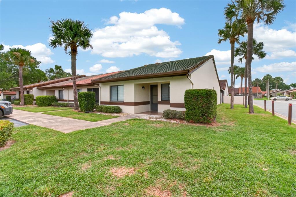 A single-story residential unit with a green tiled roof, stucco walls, and palm trees — 7360 ULMERTON ROAD UNIT 10D, LARGO, FL