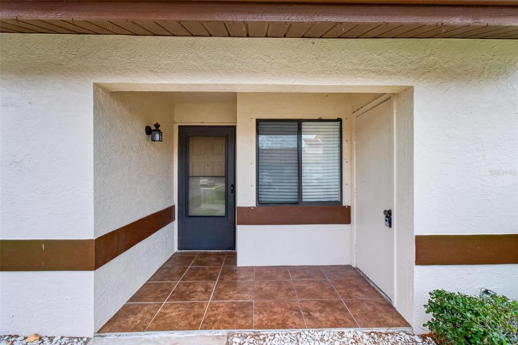 A covered entryway features a tiled porch, a dark front door, and a window — 7360 ULMERTON ROAD UNIT 10D, LARGO, FL