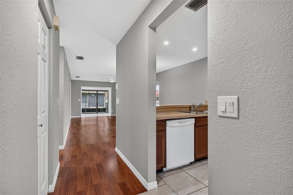 A hallway with wood flooring leads to a living area with a view of a patio — 7360 ULMERTON ROAD UNIT 10D, LARGO, FL