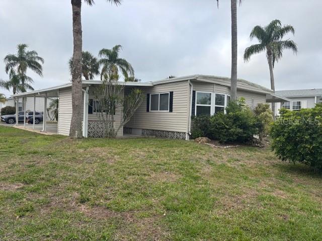 A single-story manufactured home with light siding, a carport, and palm trees on a lawn — 2100 KINGS HIGHWAY UNIT 781, PORT CHARLOTTE, FL