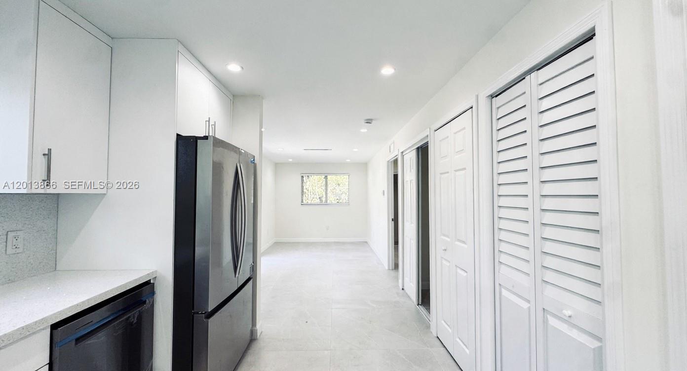 A kitchen with white cabinets and stainless steel appliances leads into an open living area — 8442 SW 107th St, Miami FL 33156, MIAMI, FL