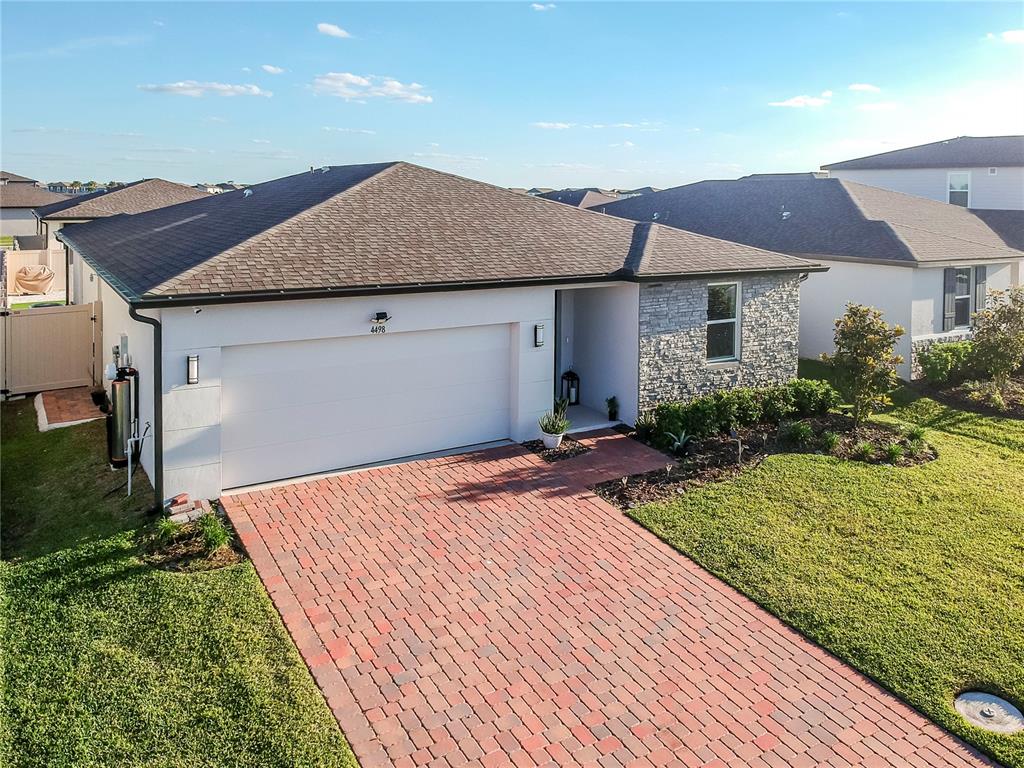 A single-story house with a white stucco facade, stone accents, and a red brick driveway — 4498 PICKEREL WEED, ST CLOUD, FL