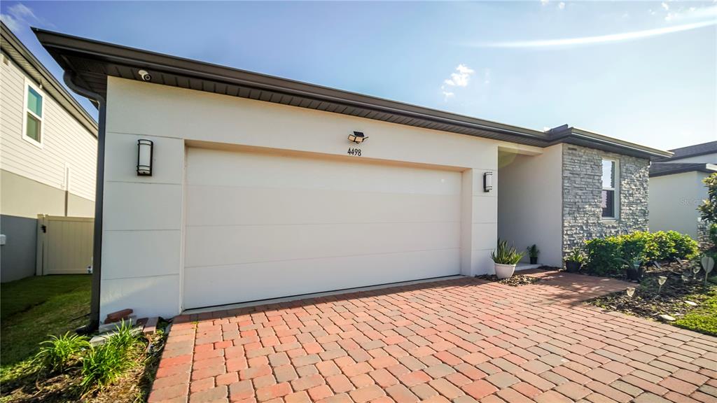 A modern house exterior features a two-car garage, a brick paver driveway, and stone siding — 4498 PICKEREL WEED, ST CLOUD, FL