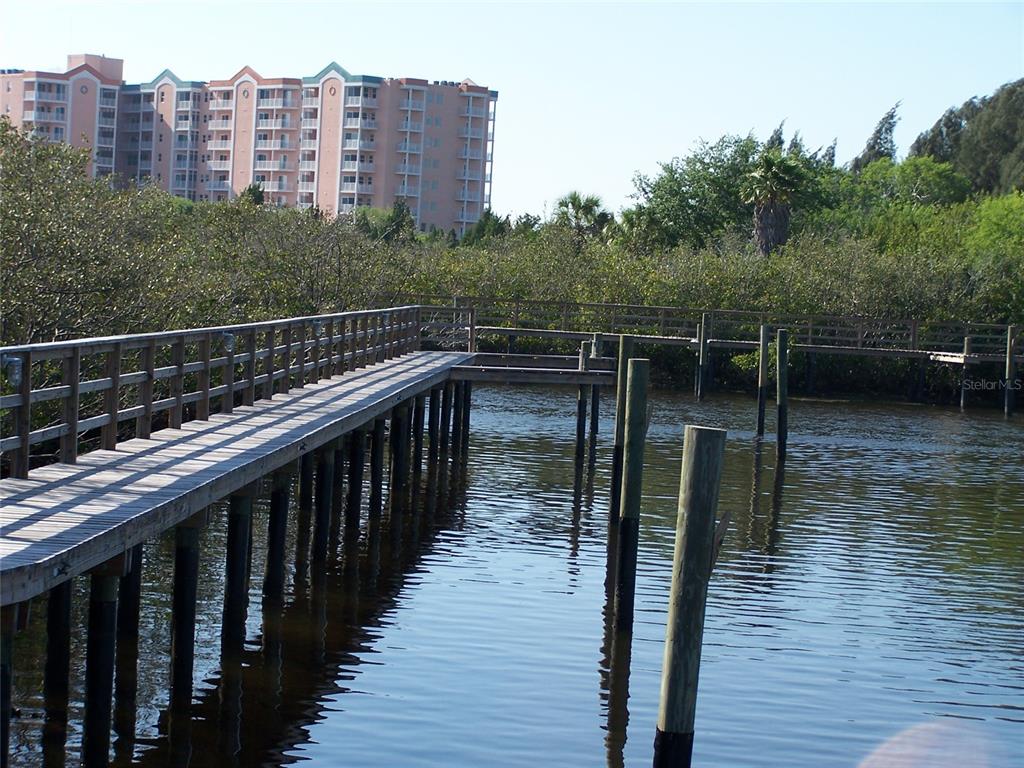 A wooden boardwalk extends over a body of water toward a large, multi-story apartment building — 0 JENNY WAY, NEW PORT RICHEY, FL