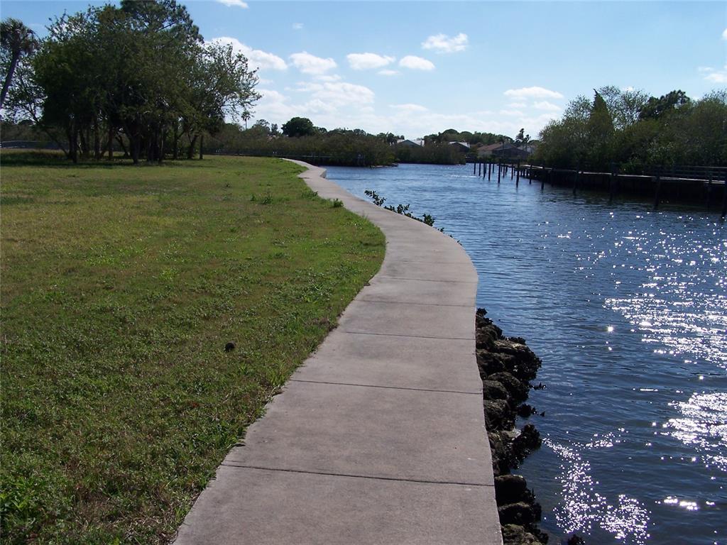 A concrete walkway curves along a grassy shoreline next to a narrow body of water — 0 JENNY WAY, NEW PORT RICHEY, FL