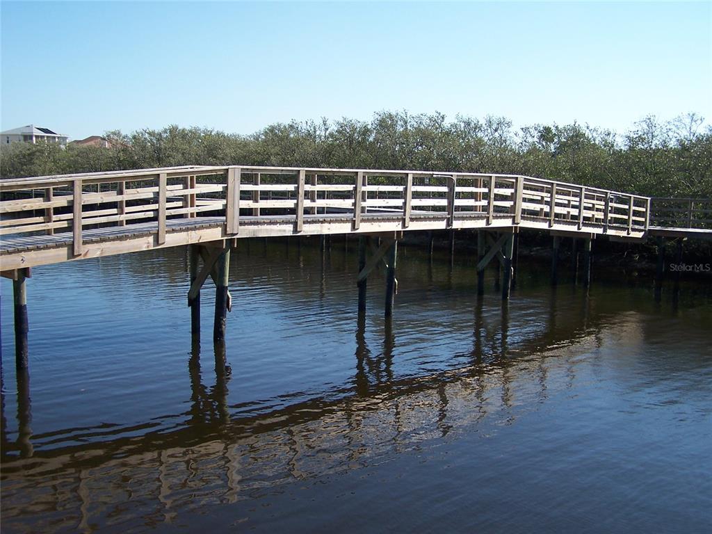 A wooden boardwalk bridge extends over calm water toward a line of coastal trees — 0 JENNY WAY, NEW PORT RICHEY, FL