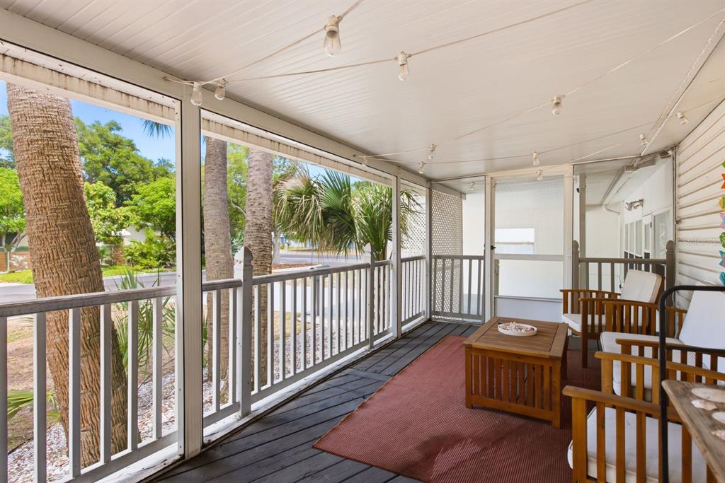 A screened-in porch features a wooden deck, outdoor furniture, and string lights overlooking palm trees — 7201 5TH AVENUE N, ST PETERSBURG, FL