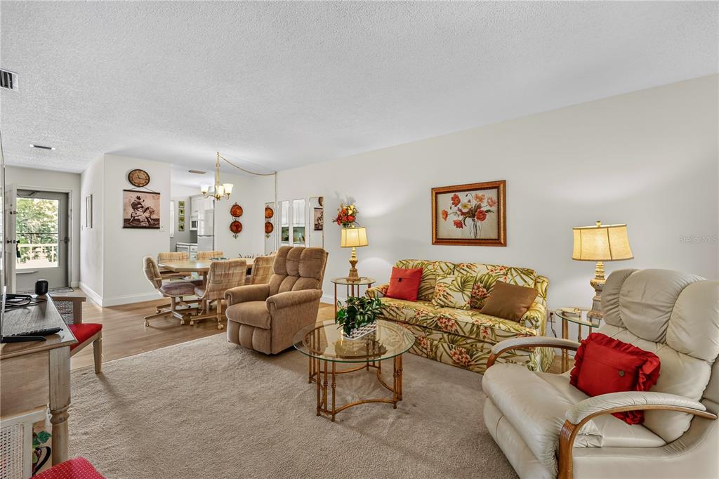 A living room with beige carpet, a floral sofa, two recliners, and an adjacent dining area — 4801 AIRPORT ROAD UNIT 119, ZEPHYRHILLS, FL