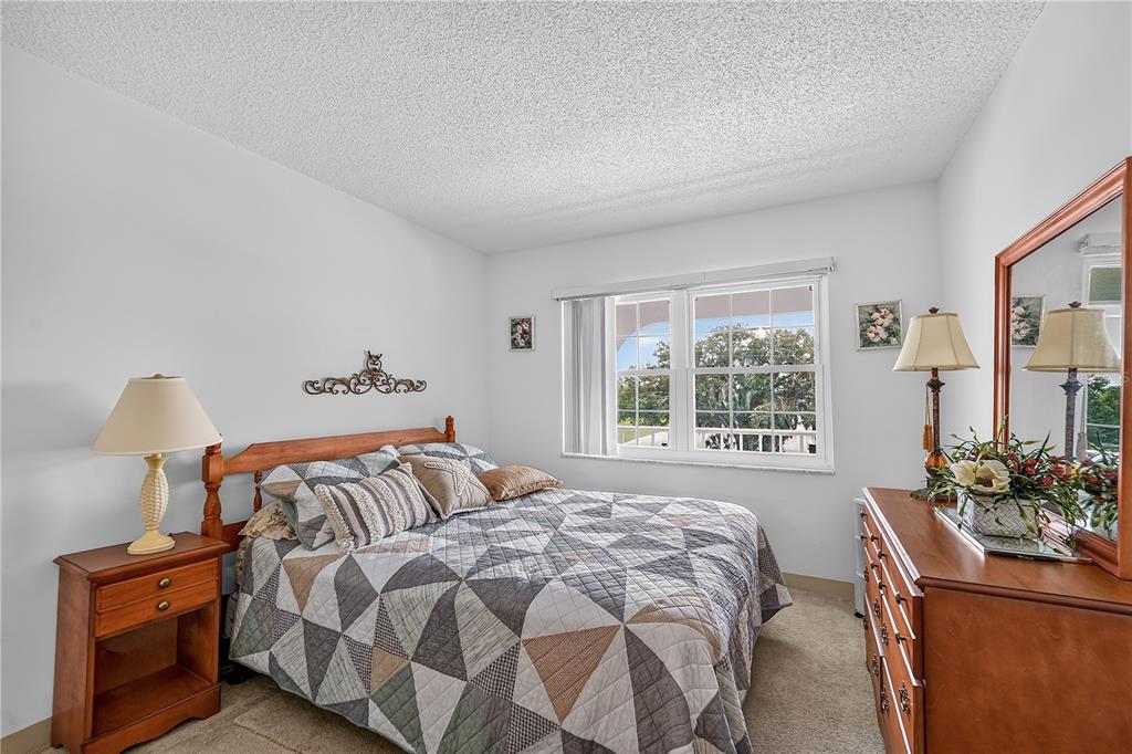 A bedroom features a bed with a geometric quilt, a wooden dresser, and a window — 4801 AIRPORT ROAD UNIT 119, ZEPHYRHILLS, FL