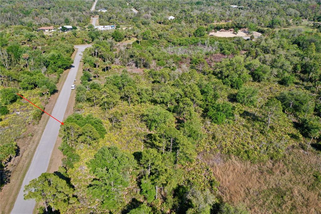 An aerial view shows a paved road running alongside a wooded, undeveloped plot of land — 12453 KOENIG LANE, PORT CHARLOTTE, FL