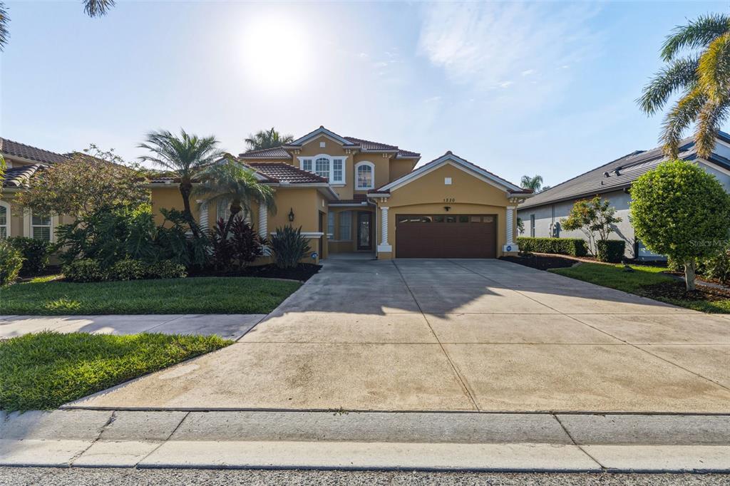 A two-story yellow stucco house features a tile roof, a two-car garage, and landscaping — 1230 CREEK NINE DRIVE, NORTH PORT, FL