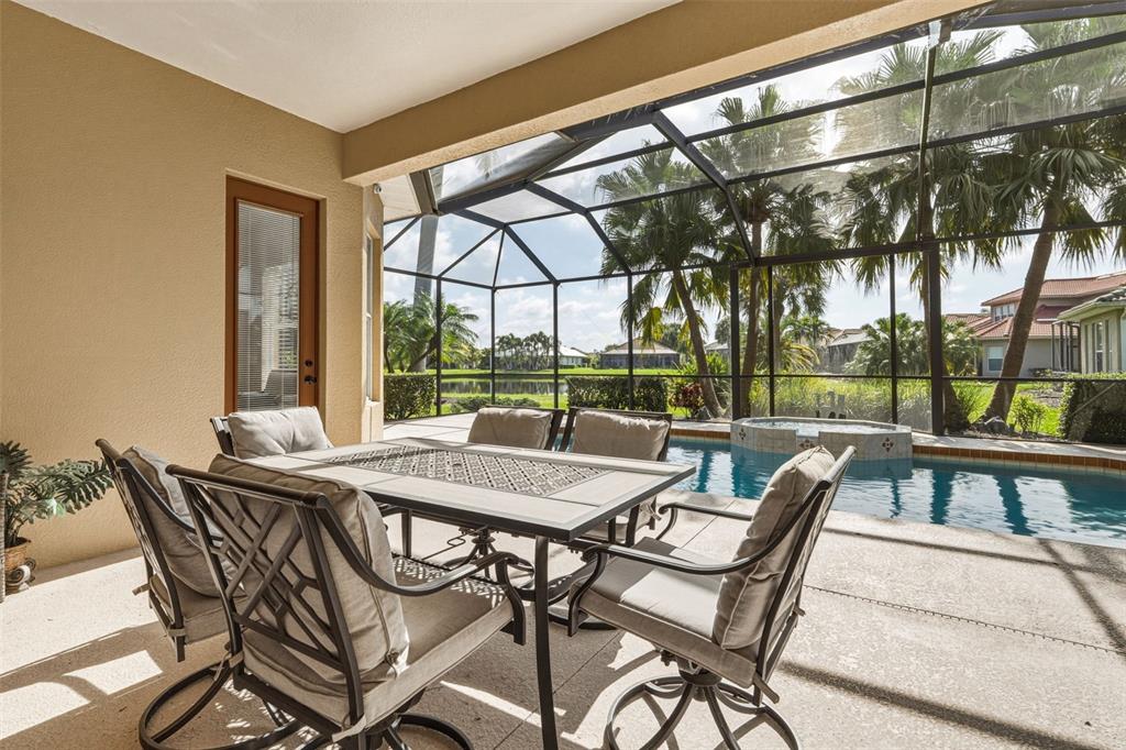 A covered patio features a dining set, a screened-in pool, and a view of palm trees — 1230 CREEK NINE DRIVE, NORTH PORT, FL