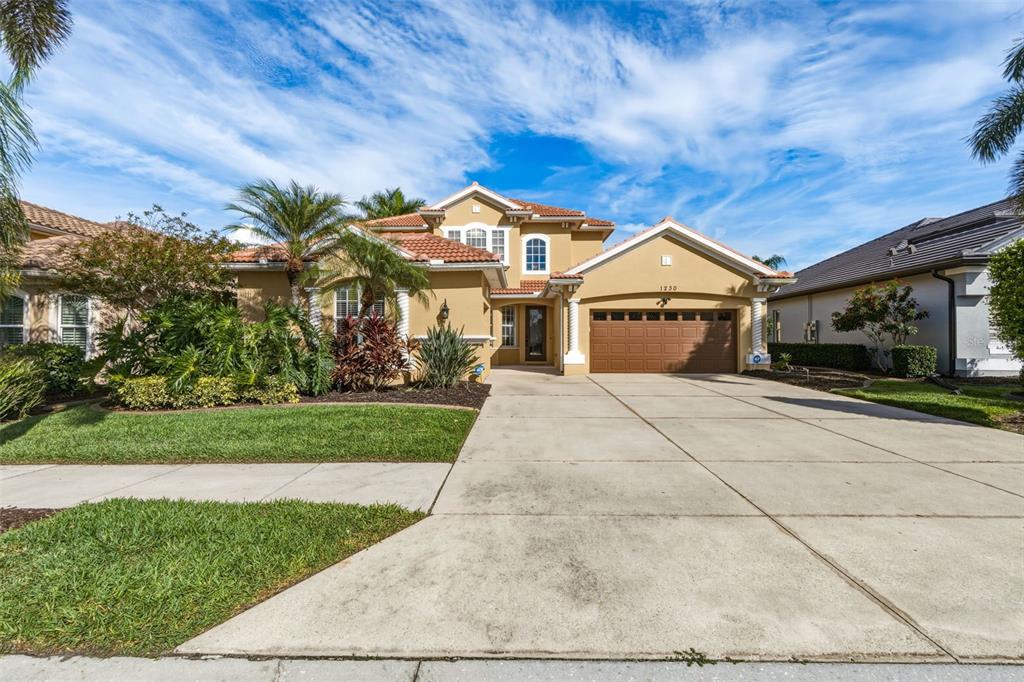 A two-story tan stucco house with a tile roof and a three-car garage — 1230 CREEK NINE DRIVE, NORTH PORT, FL