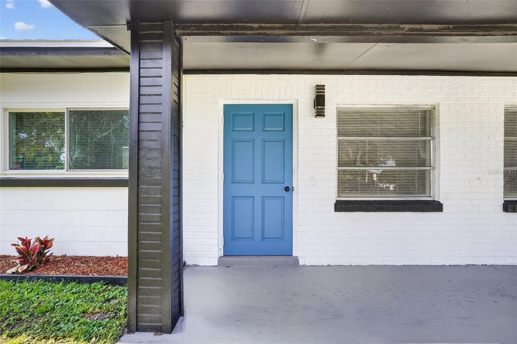 A blue front door is centered on a white brick exterior with a covered porch — 3034 TOURAINE AVENUE, ORLANDO, FL