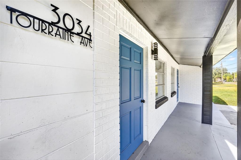 A white brick exterior wall features a blue door and a covered porch area — 3034 TOURAINE AVENUE, ORLANDO, FL