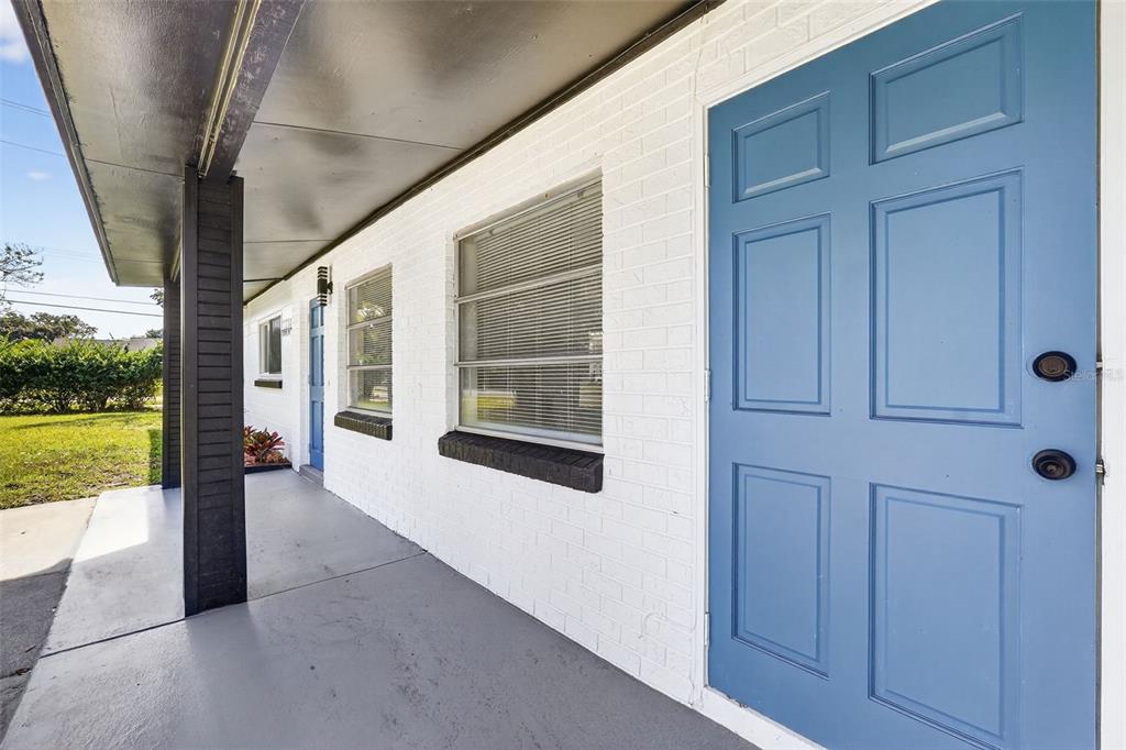 A covered porch with a blue door, white brick walls, and a dark support column — 3034 TOURAINE AVENUE, ORLANDO, FL