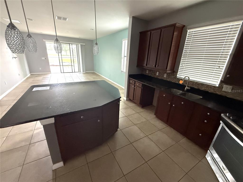 A kitchen features dark wood cabinets, black countertops, tile flooring, and a large center island — 1890 ALTAVISTA CIRCLE, LAKELAND, FL