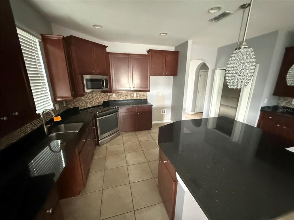 A kitchen features dark wood cabinets, black granite countertops, stainless steel appliances, and tile flooring — 1890 ALTAVISTA CIRCLE, LAKELAND, FL